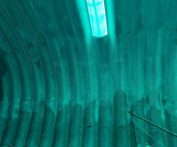 A tunnel with a green light shining through the ceiling, illuminating the underground passage.